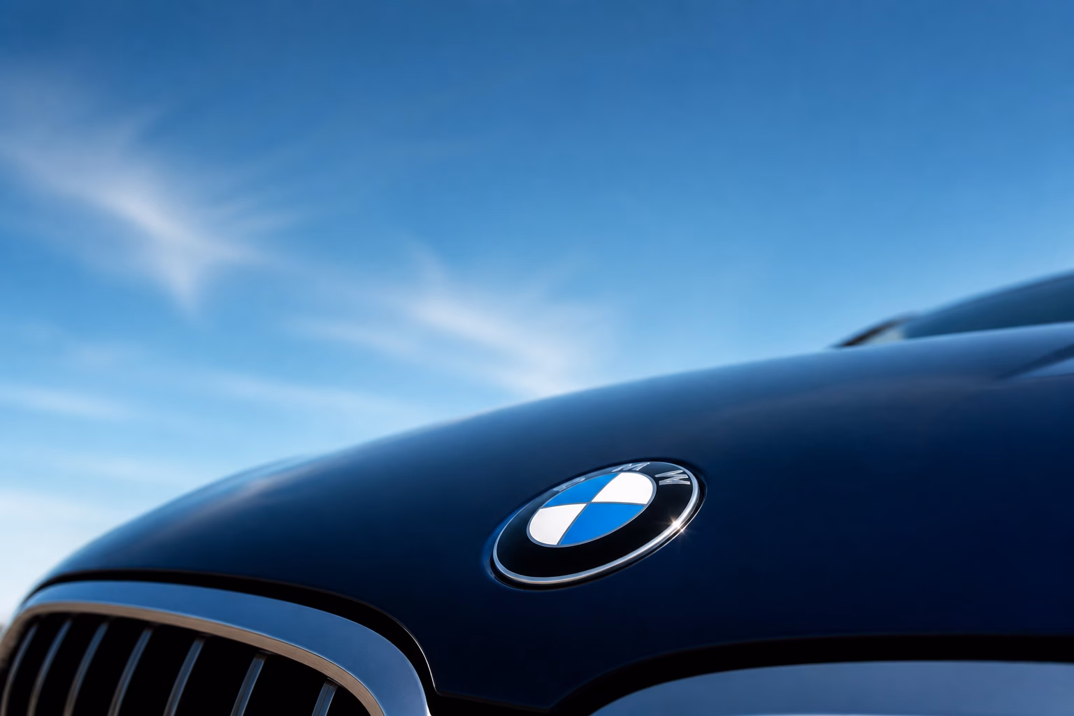 Емблема BMW на капоті синього автомобіля на тлі неба