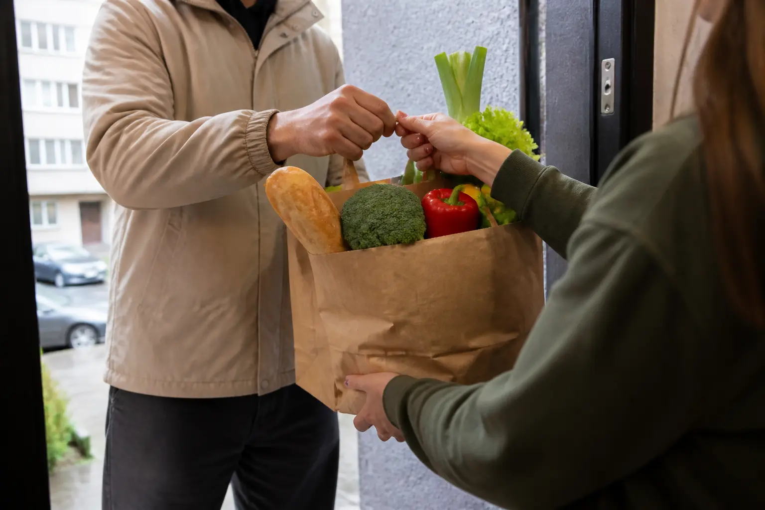 Кур'єр передає пакети з продуктами клієнту біля під'їзду